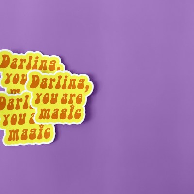 Self love sticker with funky retro font text that says "Darling, you are magic" in orange with a yellow outline