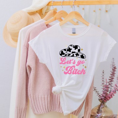 White shirt with let's go bitch text in pink with gold metallic stars and a black cowgirl hat